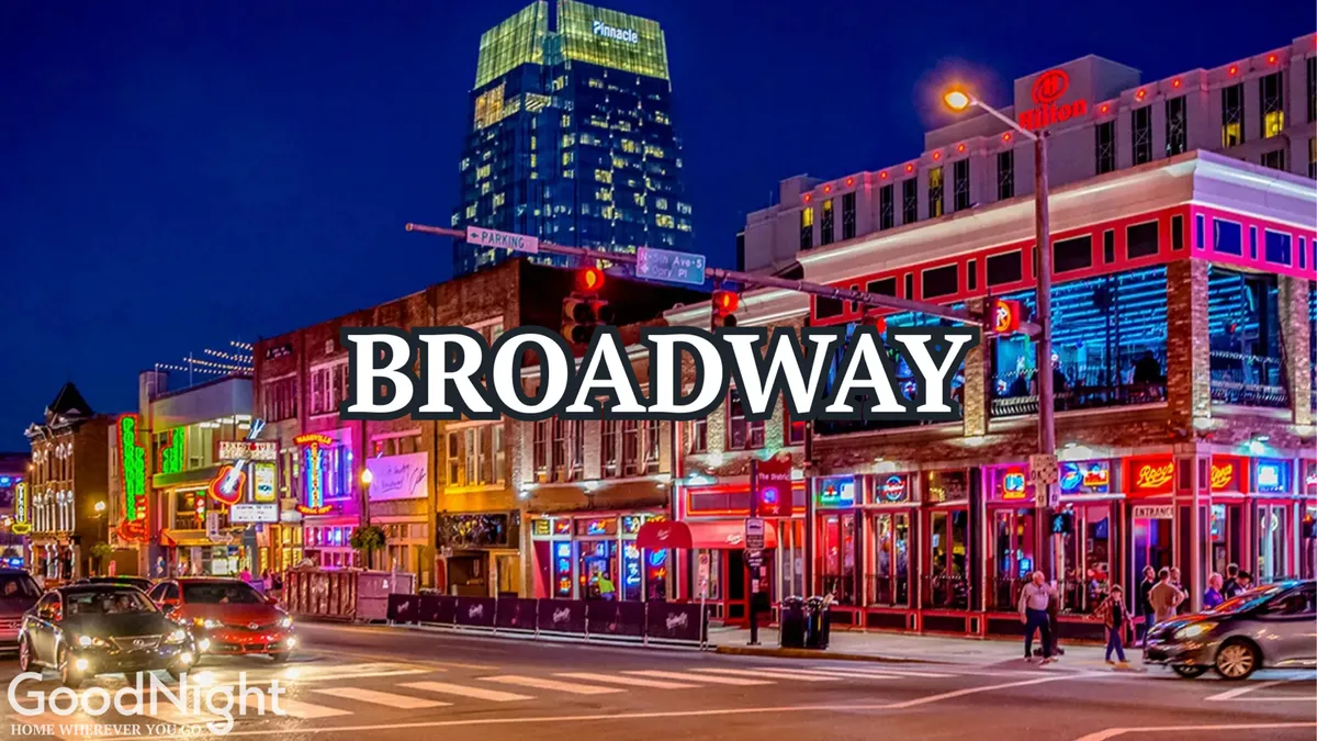A lively city street scene at night featuring vibrant neon signage, bustling restaurants and bars, people walking along the sidewalks, and a general atmosphere of energy and excitement. The image captures the electrifying nightlife and live music ambiance that Nashville is known for.
