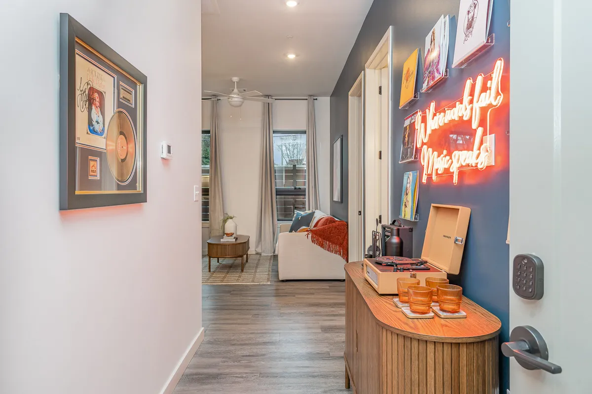 This image features a creative and cozy living area with a neon sign that reads 'Where Words Fail, Music Speaks,' a record player, gold record, comfortable couch with a throw blanket, and vibrant artwork on the walls. The space is decorated with music-themed elements that nod to Nashville’s heritage.