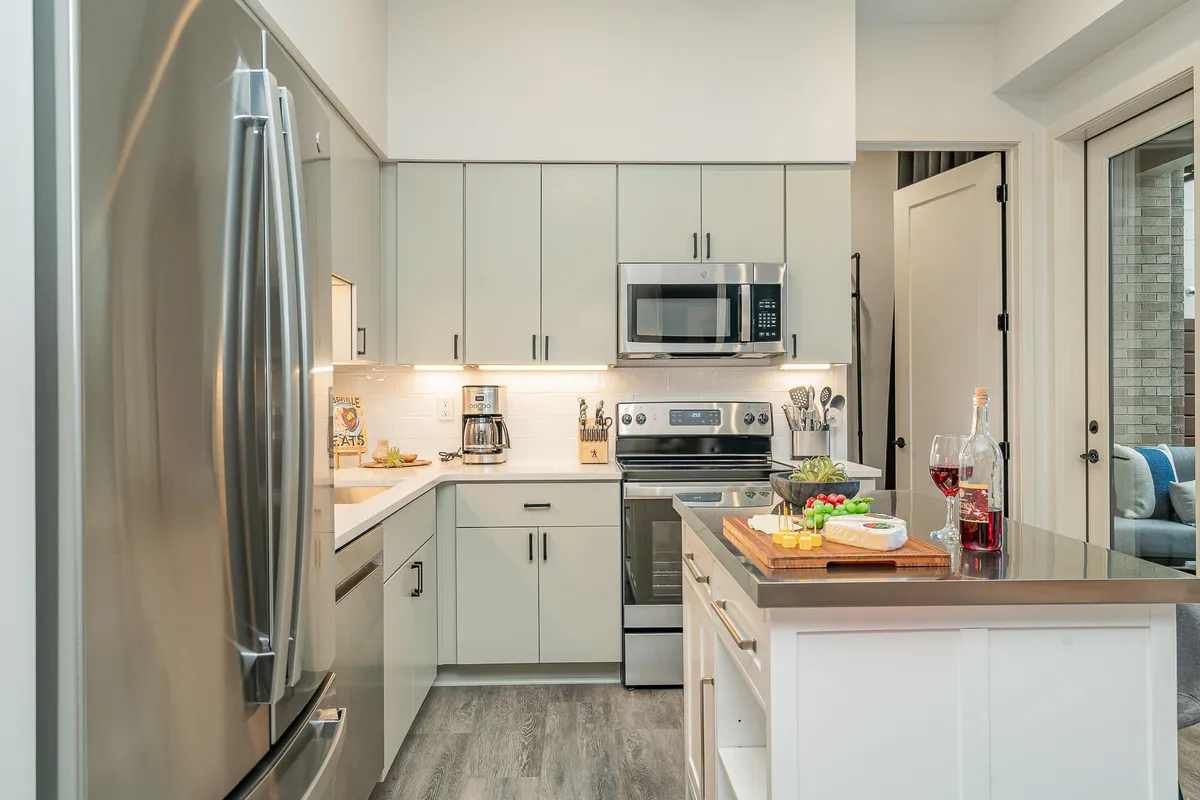 A bright, welcoming kitchen boasting stainless steel appliances, a kitchen island with a cutting board, a fresh fruit and cheese platter, and modern cabinetry. The scene conveys a sense of gathering and culinary creativity, ideal for entertaining or sharing meals.
