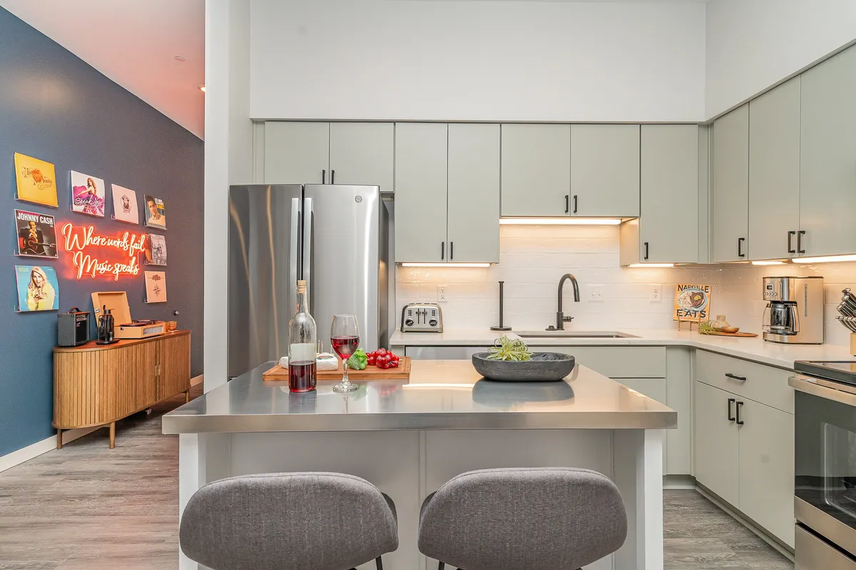A stylish, sunlit kitchen with a spacious island and chic bar stools, accented by vibrant wall art and thoughtful countertop details, inviting guests to gather, cook, and socialize.