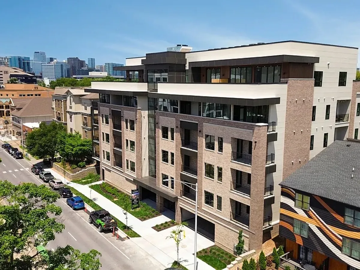 A street-level view of a modern apartment building surrounded by lush greenery, with the city skyline visible in the background. The scene highlights the property’s contemporary design and vibrant urban location, illustrating easy access to local attractions and medical facilities.