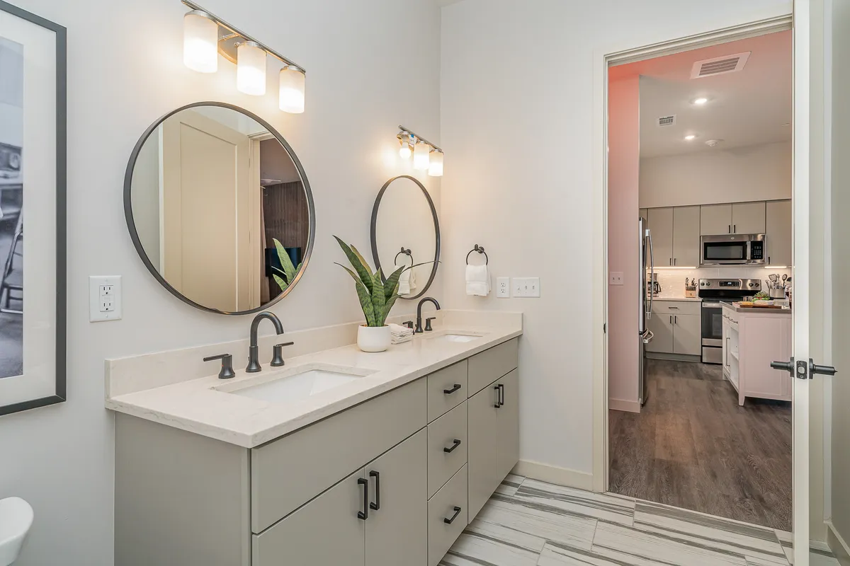 A spa-inspired bathroom with dual sinks, expansive mirrors, and a touch of greenery, evoking a fresh and calming ambiance. The layout is both luxurious and practical, ideal for morning or night routines.