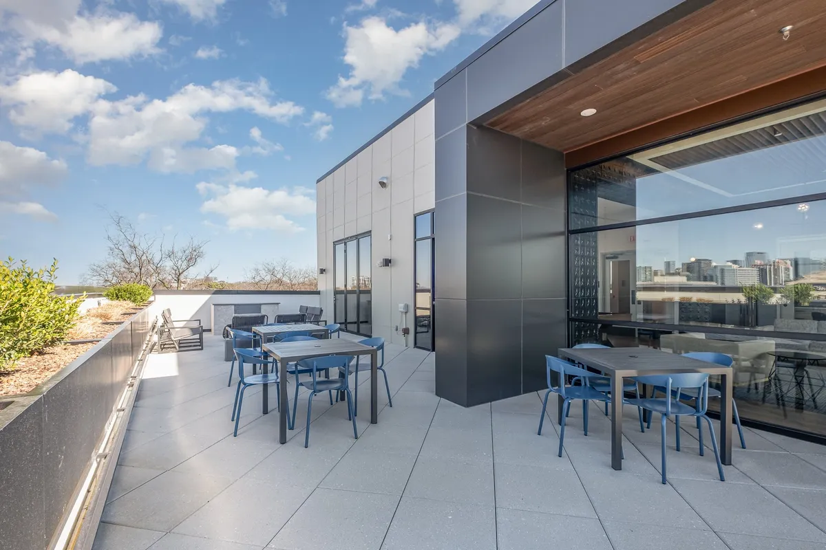 A stunning rooftop terrace with contemporary outdoor seating, lush planters, and panoramic city skyline views. The space is perfect for socializing, dining al fresco, or simply relaxing above the city as the sun sets.