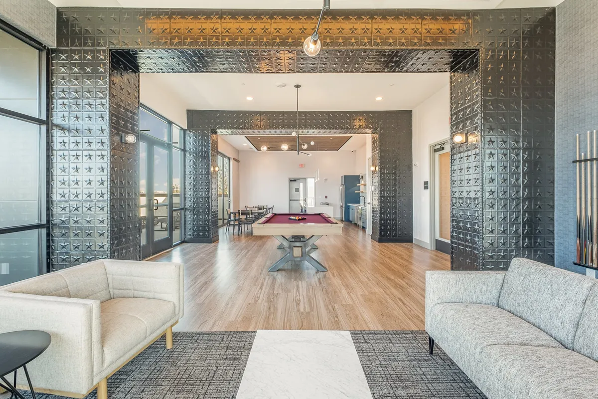 An inviting interior with a pool table, comfortable seating area, large windows letting in natural light, and a stylish decorative wall. The mood is social and casual, suggesting friendly competition and shared enjoyment within a beautifully designed space.
