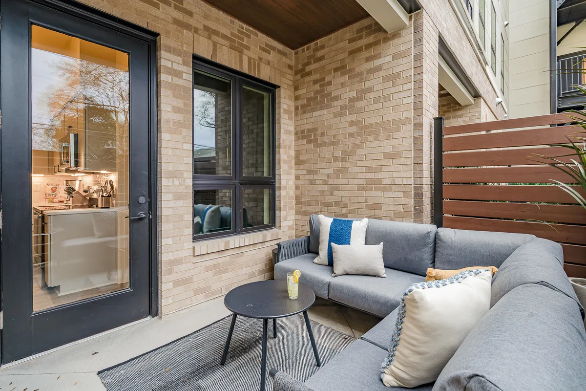 A cozy exterior seating area featuring a small table with decorative cushions, placed just outside an entrance door. The space is intimate and perfectly suited for relaxing, entertaining, or enjoying a sunny brunch. The arrangement conveys privacy and the comfort of a personal outdoor retreat.