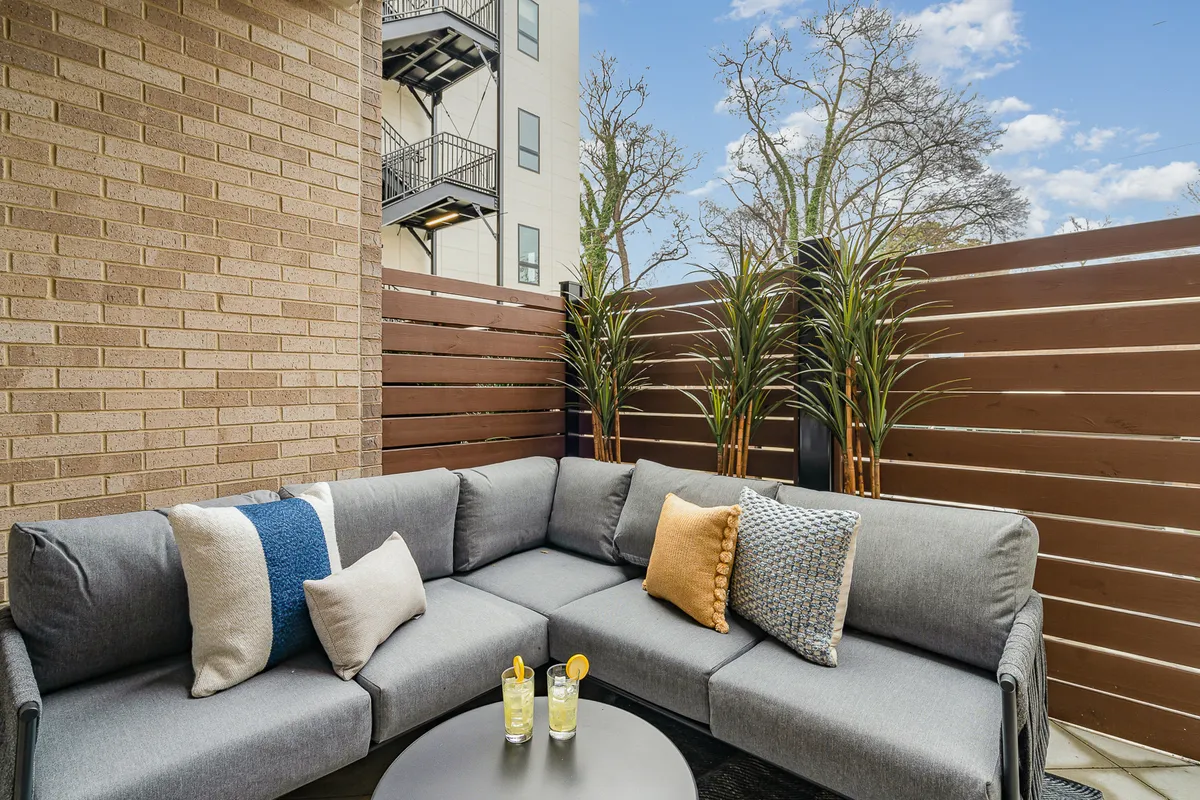 An inviting exterior rooftop lounge area with a sectional sofa, decorative pillows, drinks on the table, and lush potted plants. The elevated setting offers a relaxing spot for evening gatherings, with city views and an atmosphere perfect for unwinding after a day out.