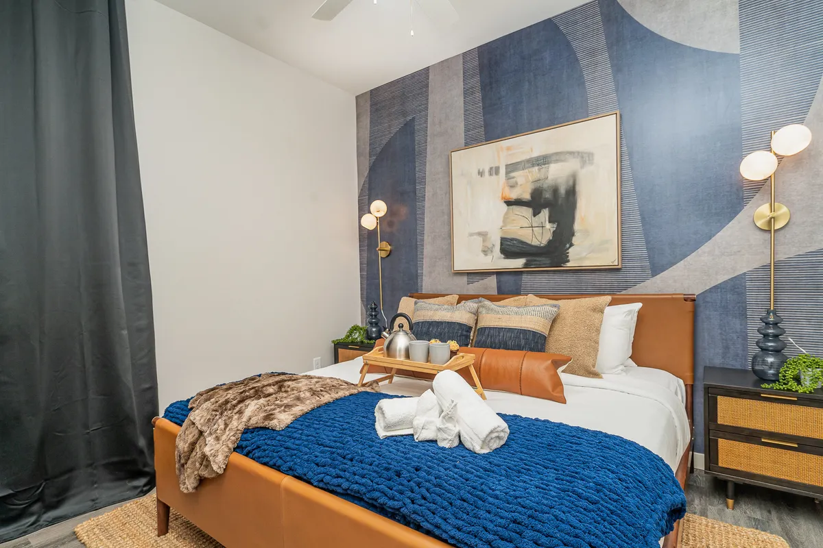A secondary bedroom space showcasing a full-sized bed with textured blankets, abstract wall art, and a decorative nightstand. The modern and comfortable decor creates an inviting space suitable for guests or family members.